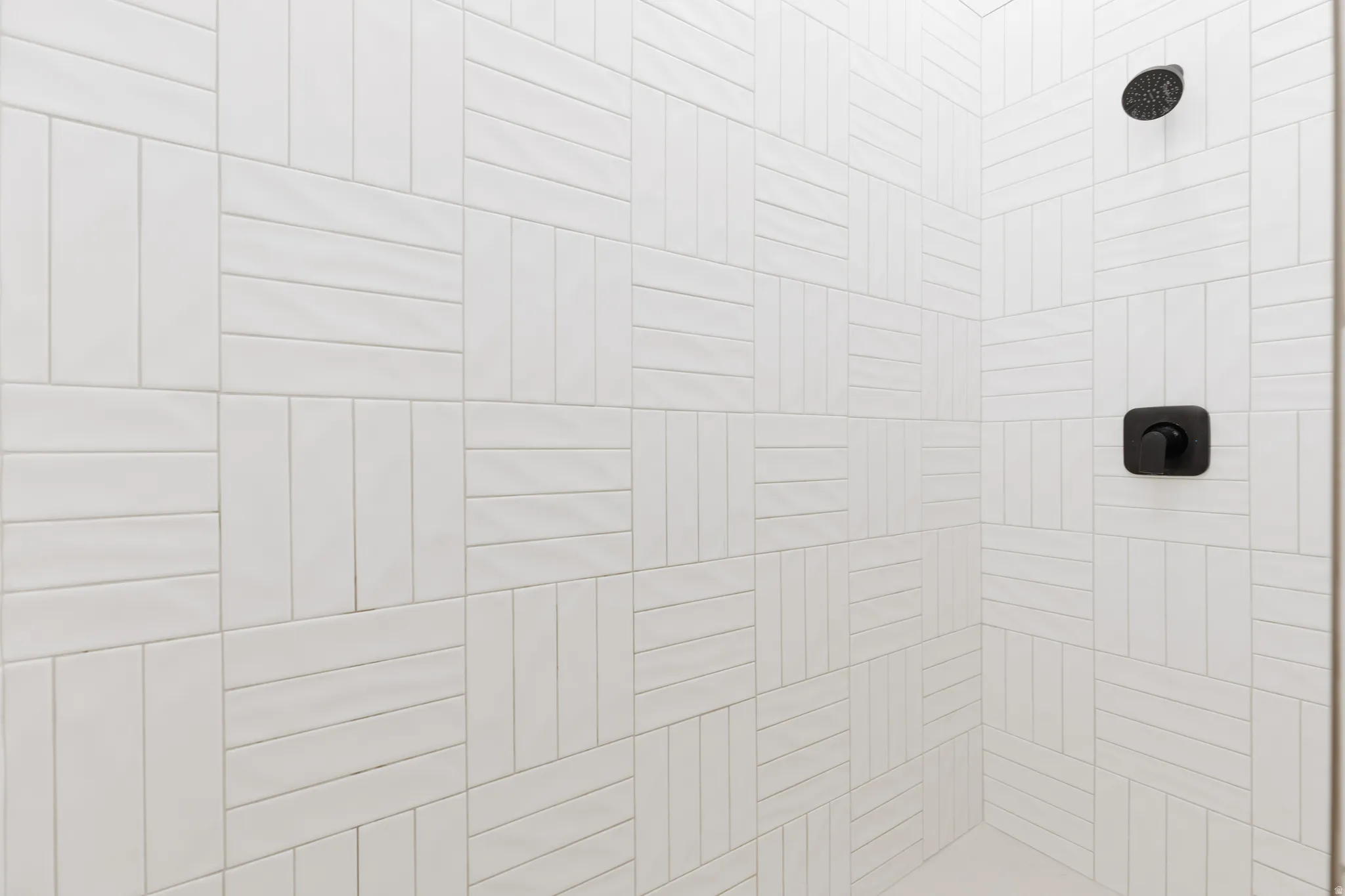 White tiled shower with a basketweave pattern, featuring a matte black shower head and control