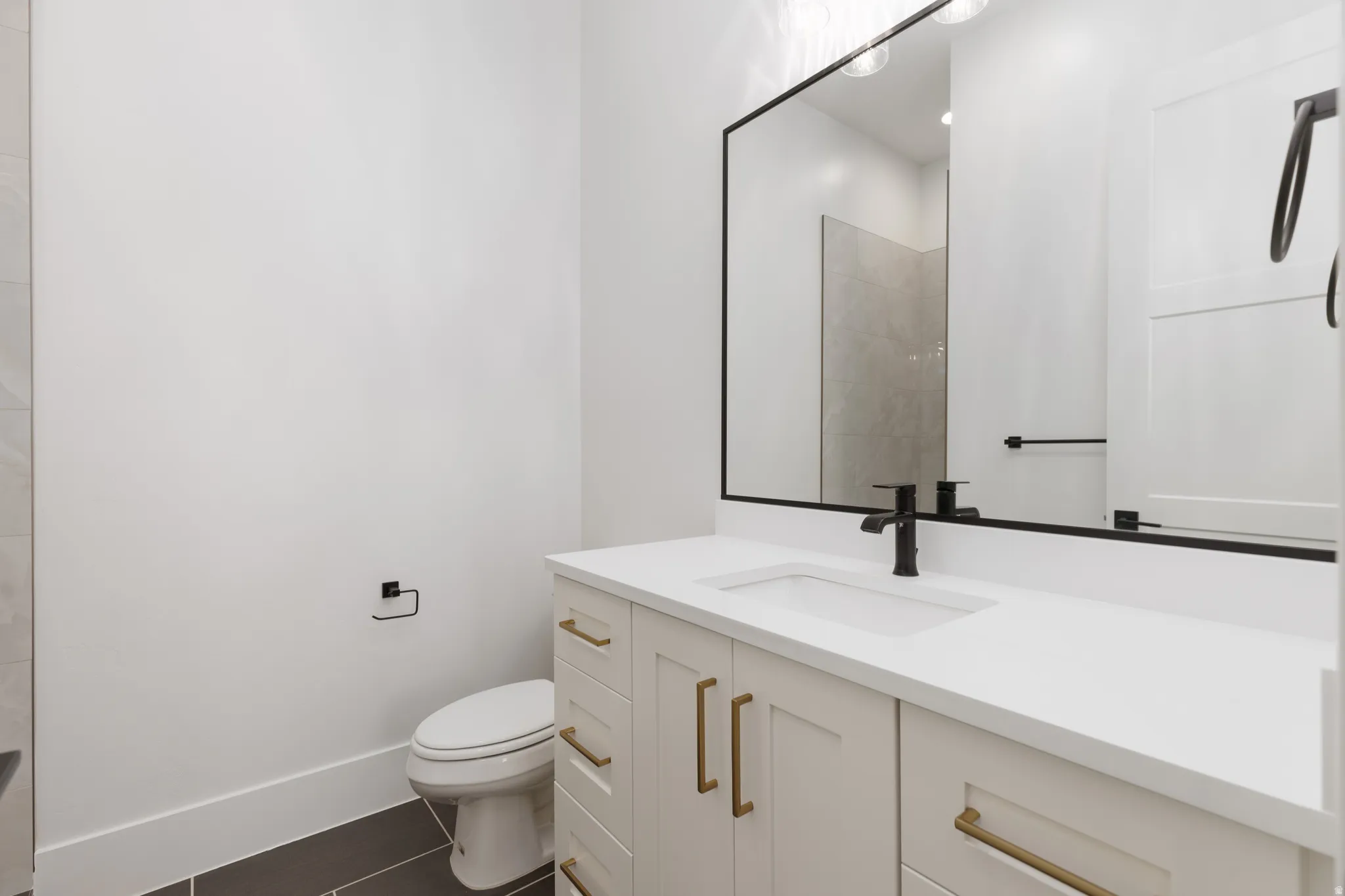 Single vanity with a white countertop and integrated sink, matte black faucet, and brass-finish hardware on cabinetry