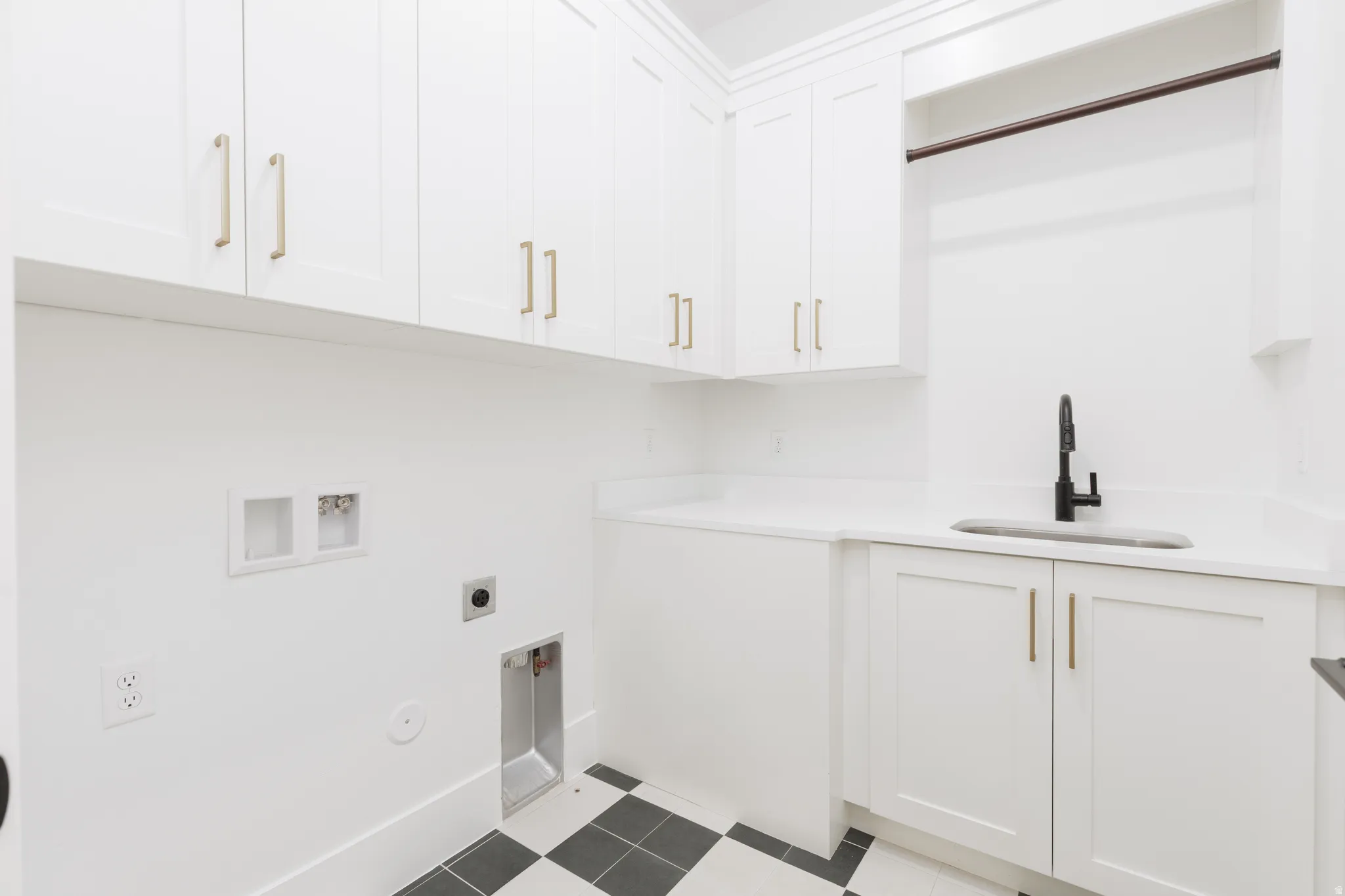 White shaker-style cabinetry with gold-finish hardware, built-in utility sink with a black faucet, white countertops, and checkerboard floor tiling