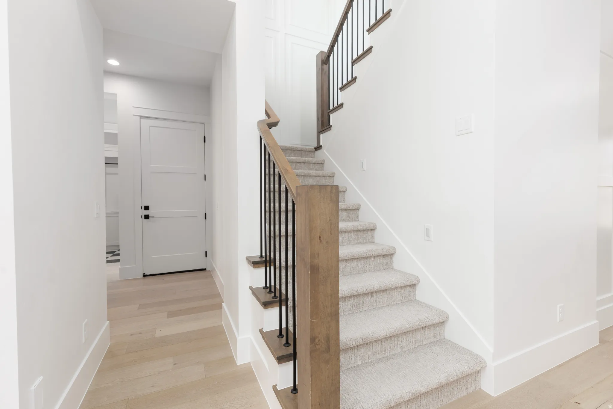 Staircase with carpeted treads and risers, wood newel posts, and wrought iron balusters