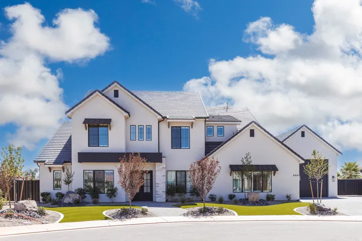 Contemporary stucco exterior with a multi-gabled roofline, black-framed windows, artificial turf landscaping, and a paver driveway