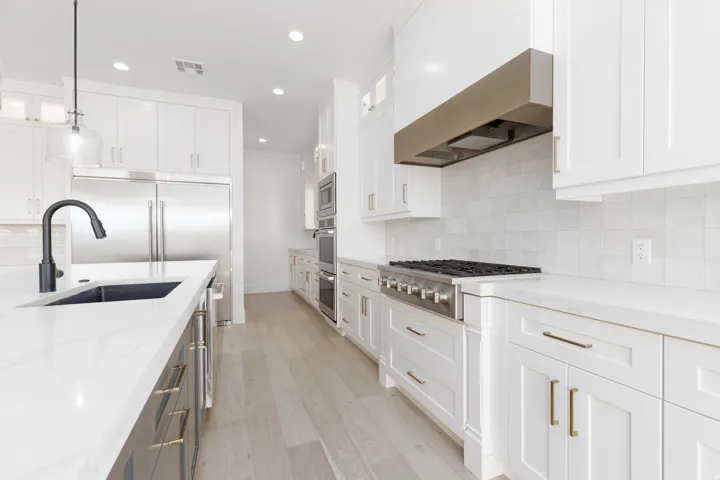 Gourmet kitchen with white cabinetry, stainless steel appliances, stone countertops, and wood-finish flooring