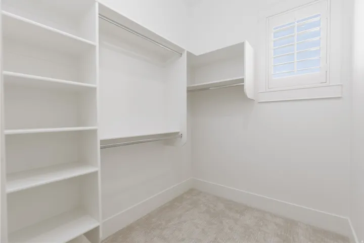 Built-in shelving, hanging rods, and a window with plantation shutters