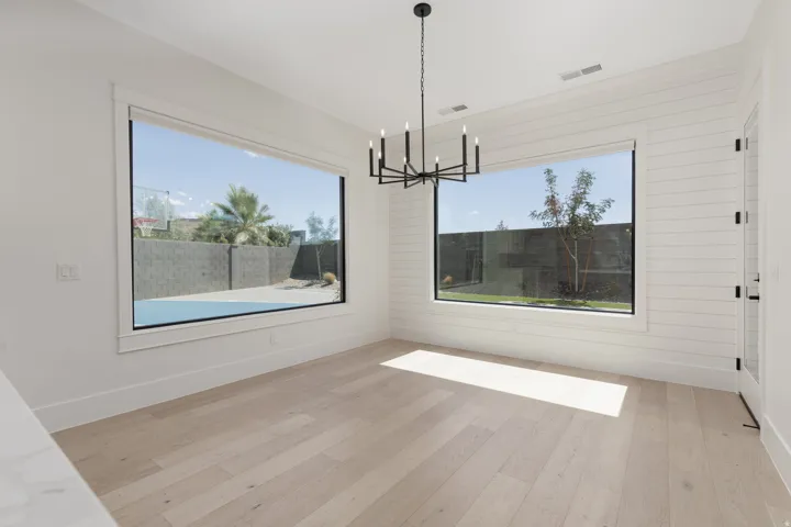 Light wood-finish flooring, two large picture windows, white shiplap wall, and a matte black chandelier
