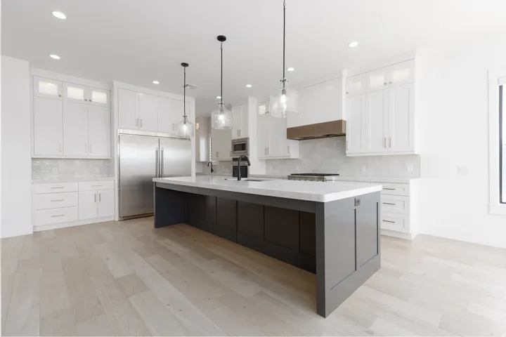 Expansive kitchen with a large center island, white shaker-style cabinetry, stainless steel appliances, and wood-finish flooring