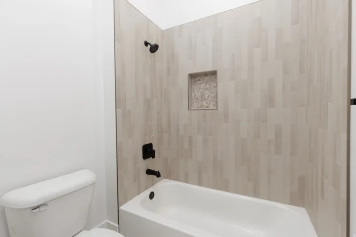 Bathtub with matte black fixtures, an integrated niche, and vertical-stacked tile surround