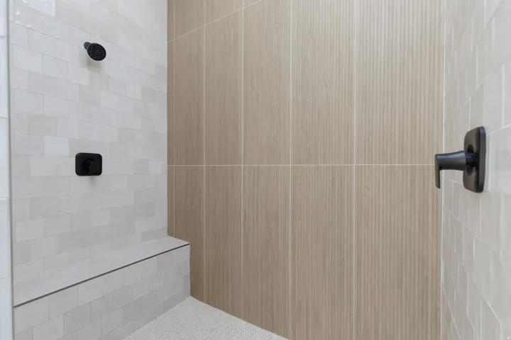 Walk-in shower with a built-in bench, matte black fixtures, and mixed tile finishes