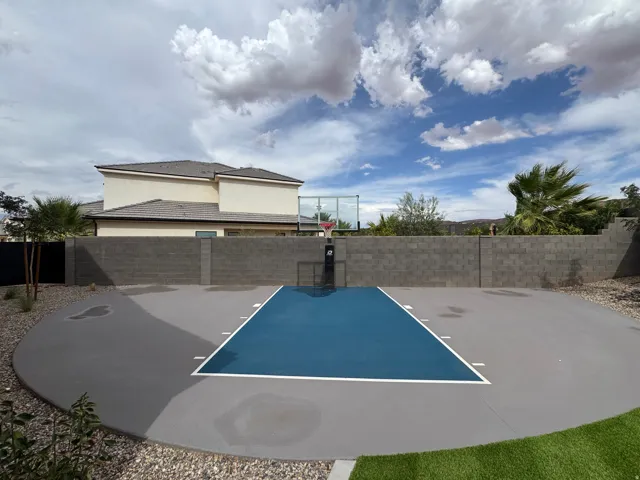 Expansive paved sport court featuring a painted playing surface and adjustable hoop, surrounded by a durable block perimeter wall