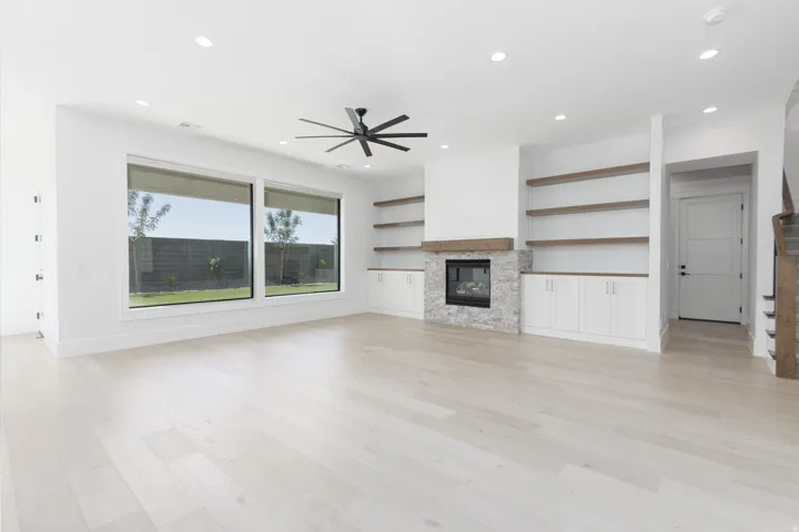Expansive great room featuring wood-finish flooring, a fireplace with stone surround and wood mantel, built-in cabinetry with open shelving, and large windows