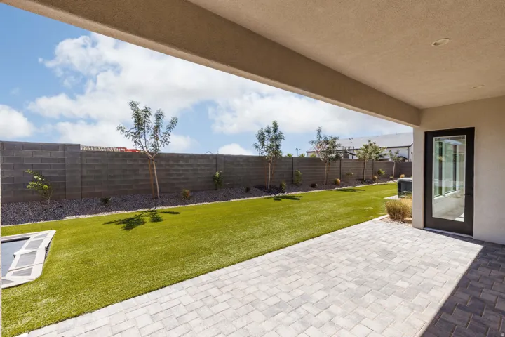 Covered patio with paver flooring, artificial turf, block wall fencing, and low-maintenance landscaping
