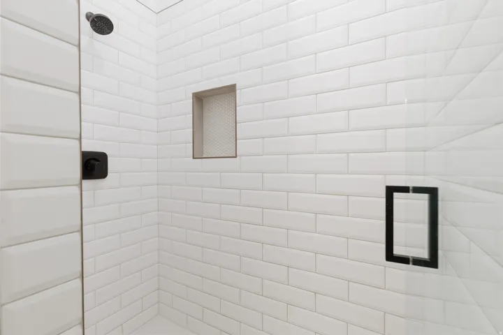 Shower enclosure featuring white subway tile, a built-in shower niche, a matte black shower head, and a frameless glass door with a matte black handle