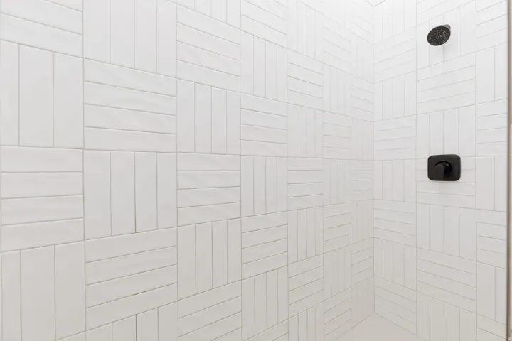 White tiled shower with a basketweave pattern, featuring a matte black shower head and control