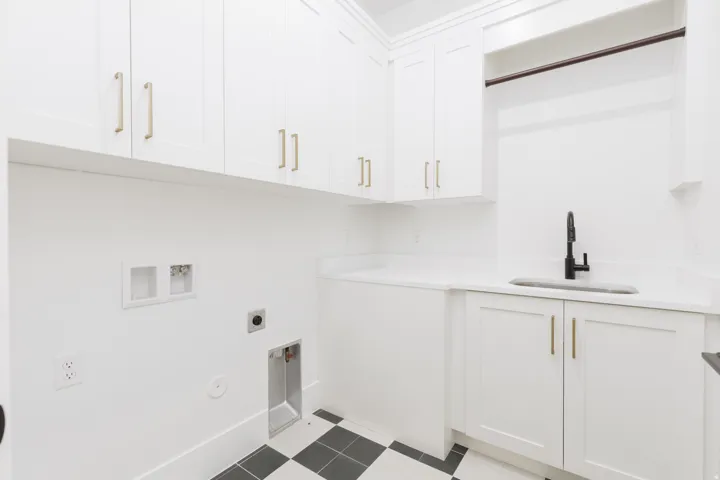 White shaker-style cabinetry with gold-finish hardware, built-in utility sink with a black faucet, white countertops, and checkerboard floor tiling