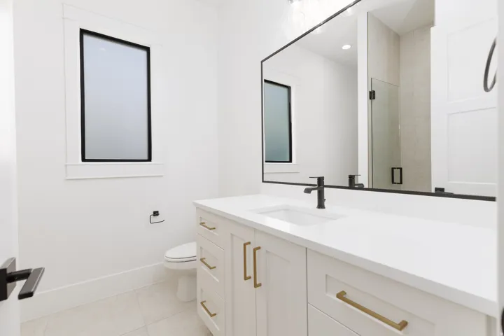 White vanity with gold-tone hardware, a rectangular undermount sink, and a black single-handle faucet