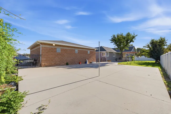 Expansive concrete patio, brick exterior outbuilding, landscaped yard, and white picket fencing