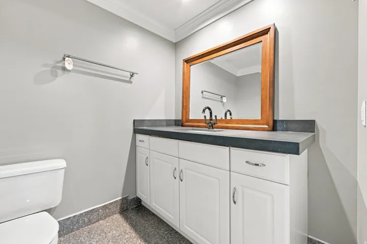 White vanity with chrome hardware, dark countertop, wood-framed mirror, and recessed lighting, and shower