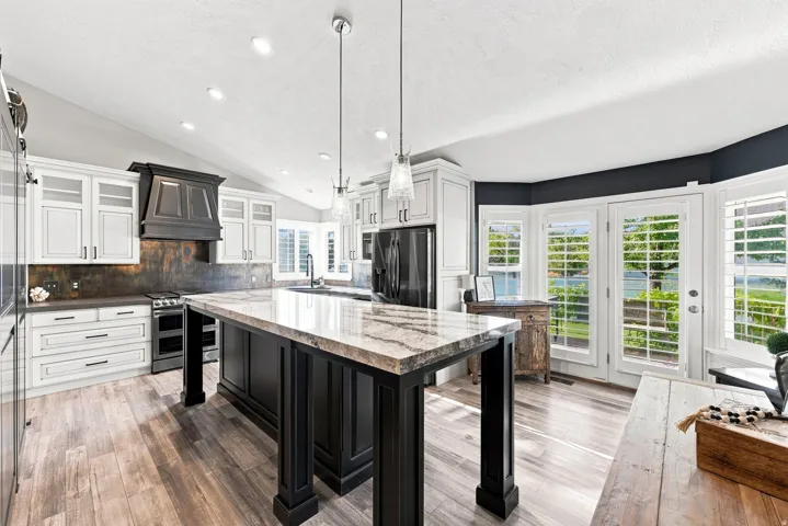 Kitchen featuring a vaulted ceiling, wood-finish flooring, two-tone cabinetry, a central island with plenty of room for entertaining.