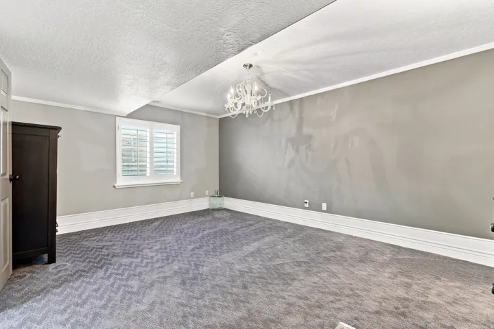 Gray textured carpeting featuring a chevron pattern, white plantation shutters, and a multi-arm chandelier