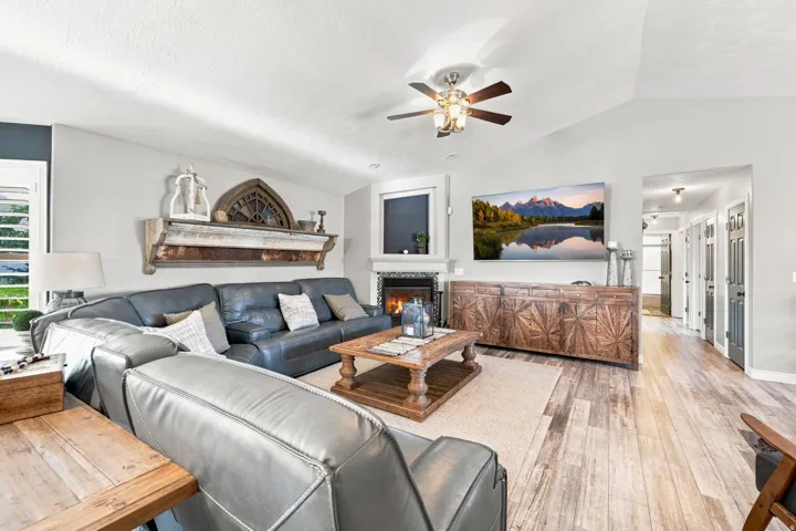 Vaulted ceiling with a ceiling fan, fireplace, wood-finish flooring, and plenty of family space.