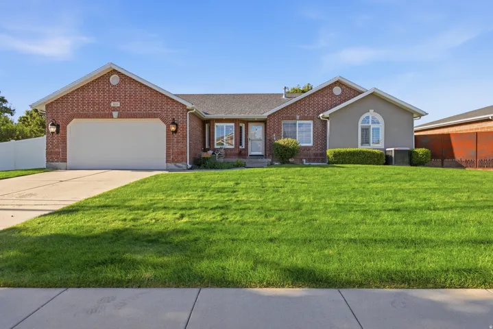 Brick facade with stucco accents, an attached garage, a concrete driveway, and a front lawn