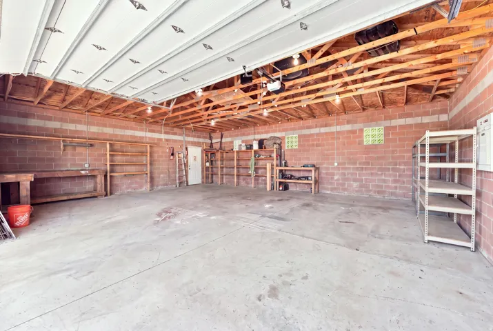 Spacious detached 4 car garage with exposed wood beam ceiling, concrete flooring, brick walls, and built-in shelving