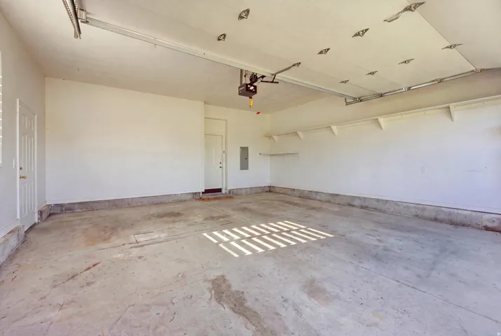 Attached 2 garage with concrete flooring, multiple access doors, and built-in wall shelving
