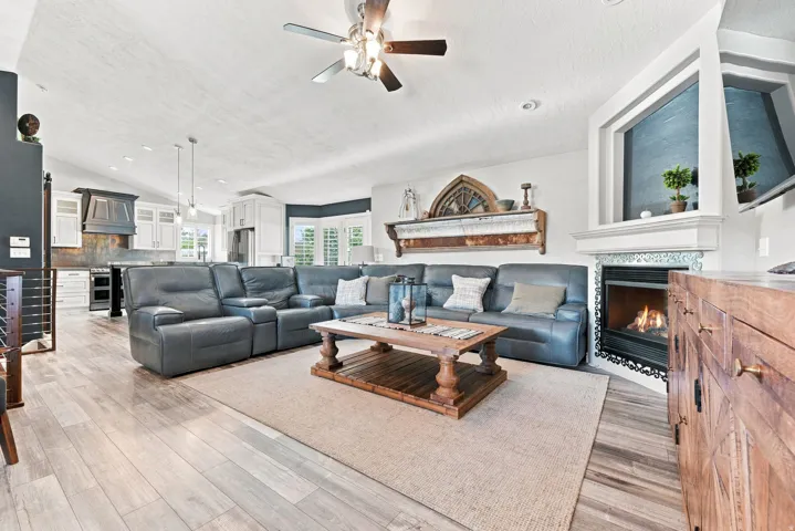 Wood-finish flooring throughout, vaulted ceiling with a ceiling fan, gas fireplace with tile surround, built-in shelving, and recessed lighting