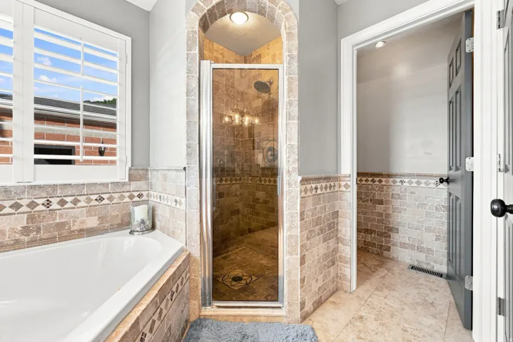 Tiled shower with glass enclosure, corner soaking tub, plantation shutters, decorative tile accents, sperate bathroom