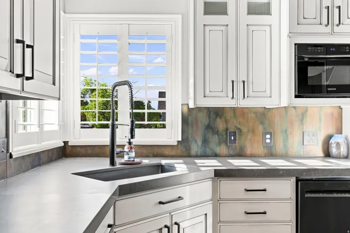 White cabinetry with dark hardware, undermount sink with a gooseneck faucet, light-toned countertops, and a built-in microwave