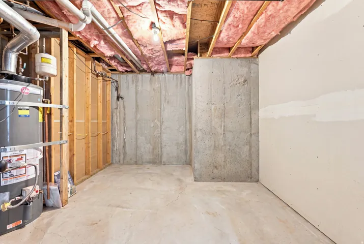 Concrete foundation walls and flooring, exposed ceiling joists with insulation, visible utility plumbing, and a water heater installation