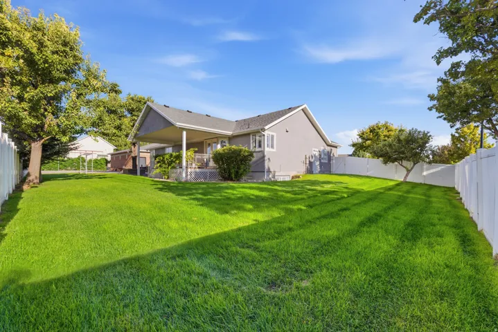 Expansive backyard featuring a manicured lawn, established trees, and a covered porch