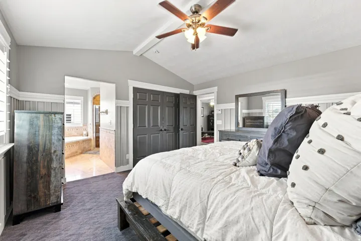 Vaulted ceiling with a ceiling fan, board and batten wainscoting, carpet flooring, and double closet doors