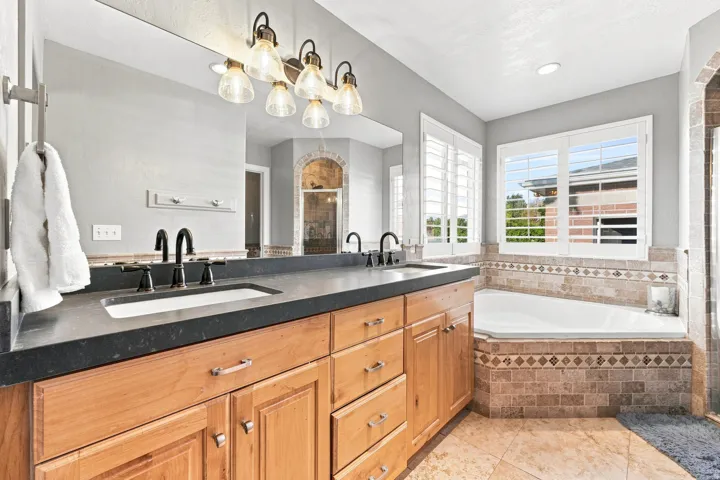 Dual sink vanity with wood-finish cabinetry and dark countertops