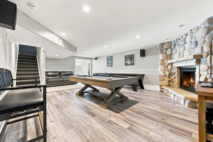Stone-clad fireplace with a hearth, wood-finish flooring, recessed lighting, and a carpeted staircase