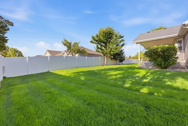 Expansive lawn featuring mature trees and a white privacy fence