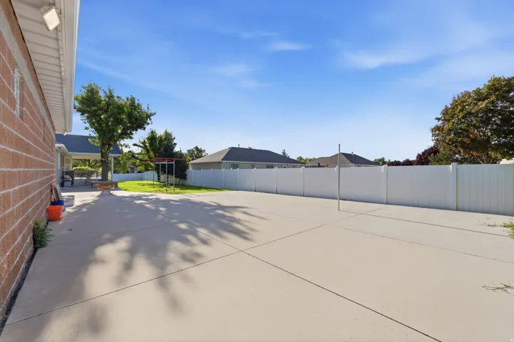 Expansive concrete patio with a white privacy fence and a manicured lawn