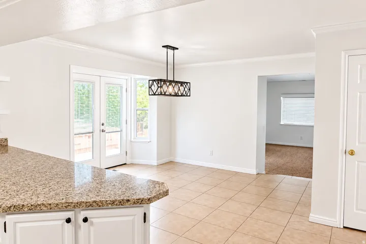Granite-style countertop, white cabinetry with dark hardware, tile flooring, modern rectangular pendant light, and double glass panel doors