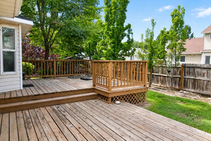 Expansive composite deck featuring multiple levels with wood-finish decking and integrated wooden railings, overlooking a landscaped yard with mature trees and lush lawn
