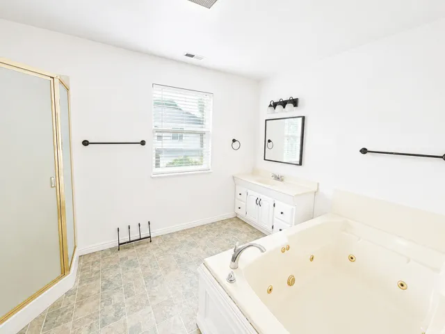Tiled flooring, white vanity with integrated sink, framed mirror, built-in jetted tub, and a corner shower with gold-tone framing