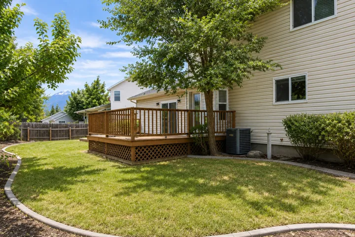 Expansive backyard featuring a wood deck with lattice skirting, a manicured lawn, and mature trees