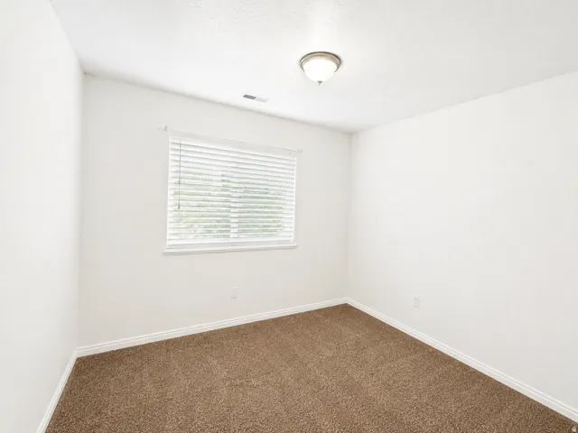 Bright secondary bedroom featuring neutral wall finishes, a picture window with horizontal blinds providing natural light, and soft carpeting throughout