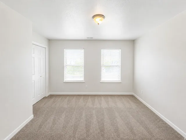 Neutral-toned wall-to-wall carpeting, dual windows with blinds, recessed closet with bi-fold doors, and a flush mount ceiling light fixture