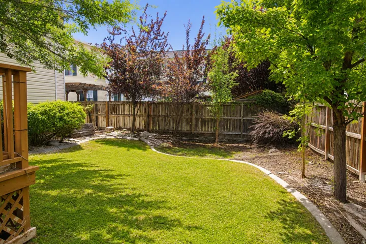Expansive backyard with a manicured lawn, established perimeter fencing, mature trees, and a wooden deck structure