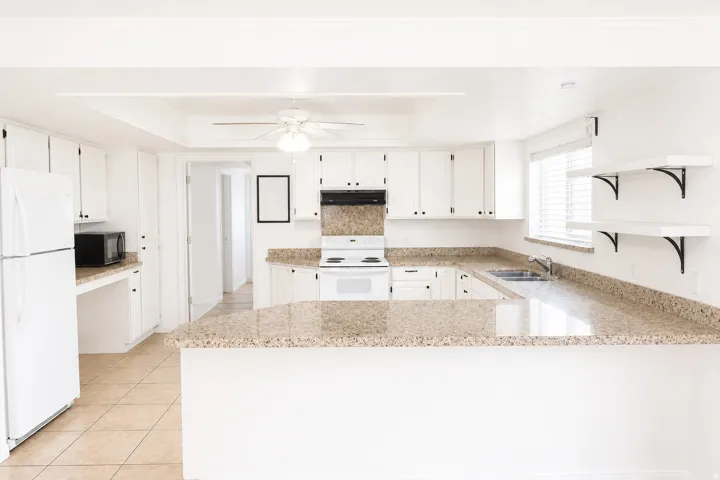 White cabinetry, U-shaped counter space, built-in sink, integrated appliances, and tile flooring