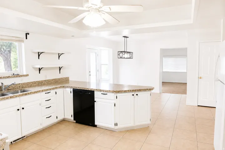 Kitchen featuring white cabinetry, granite-style countertops, an integrated dishwasher, and tile flooring