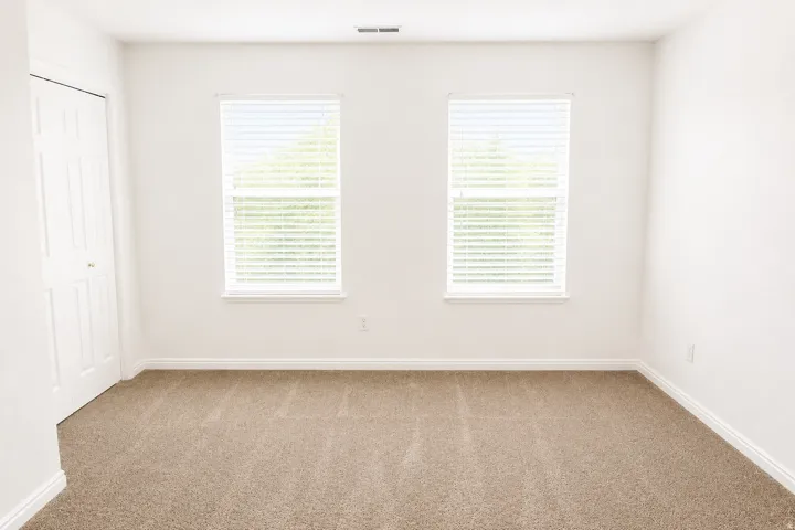 Neutral carpet flooring, white walls, two windows with horizontal blinds, and a white bi-fold closet door