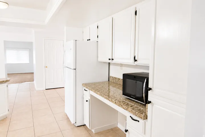 Bright galley kitchen featuring white cabinetry with black hardware, granite-style countertops, and built-in microwave