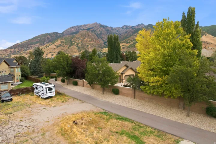 Mountain backdrop, mature trees, paved road, gravel shoulder, and a privacy wall