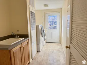 Utility room featuring a built-in sink with wood-finish cabinetry, light-toned flooring, and a glass-paneled exterior door