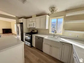 Kitchen featuring white cabinetry, light-toned countertops, wood-finish flooring, a farmhouse sink, and stainless steel appliances